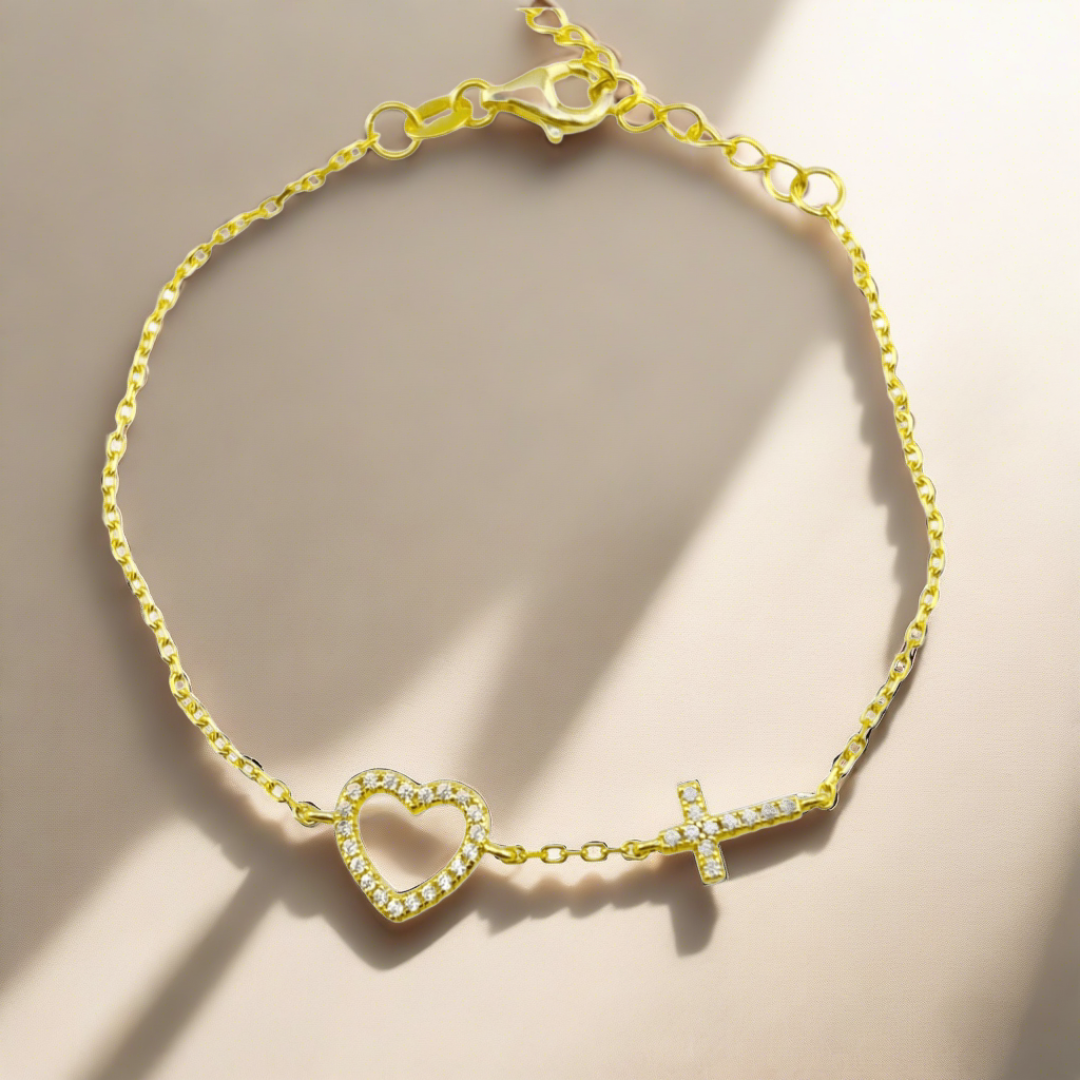 Closeup of a gold chain bracelet, dainty in thickness, with a heart charm and a cross charm  weaved into the bracelet, not dangling.