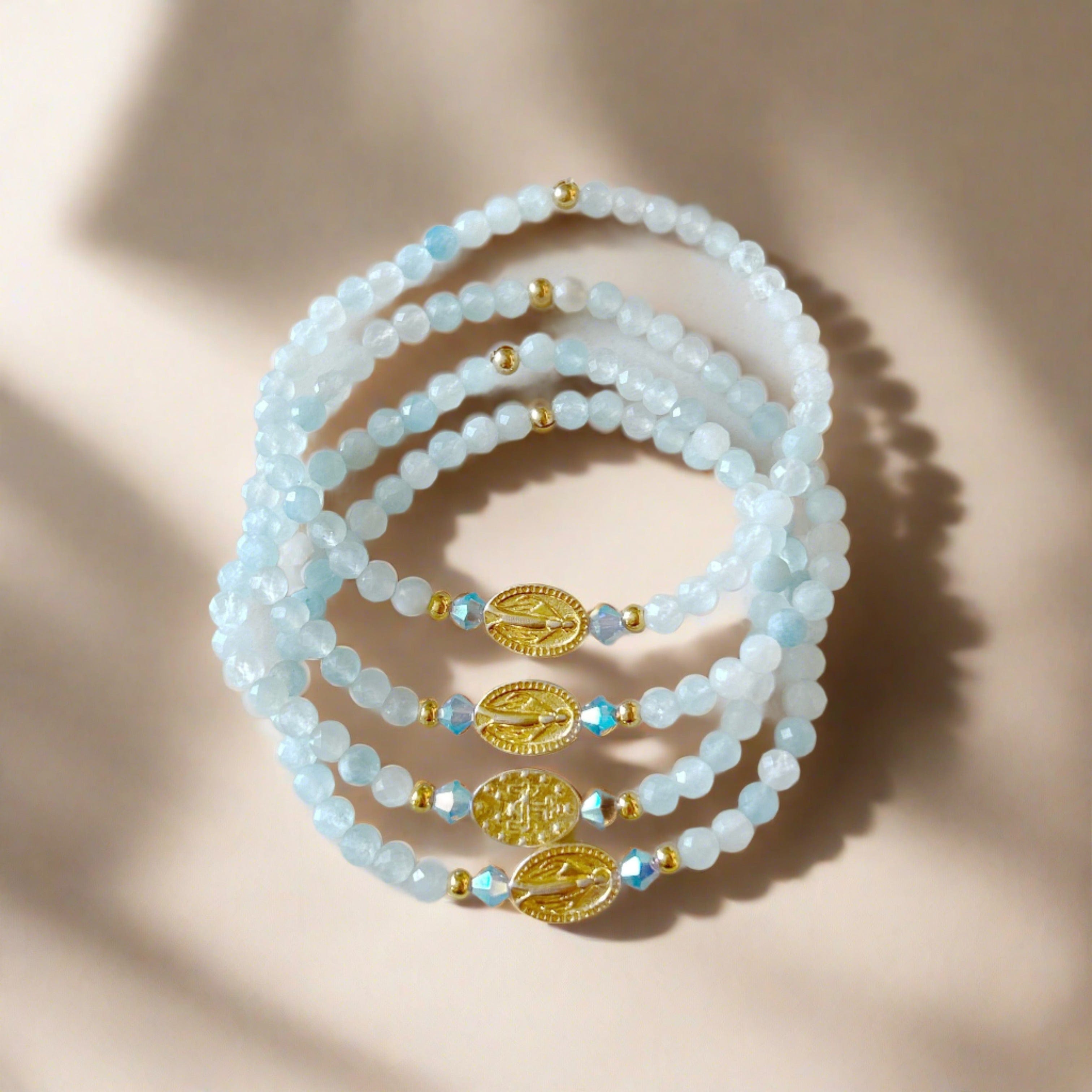 picture of a stack of beaded bracelets with virgin mary charm in center against a tan soft lit background