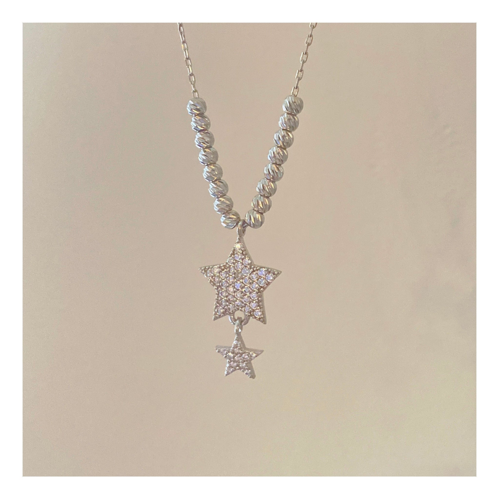 close up of the center of this necklace, has diamond cut rhodium over sterling silver gold beads , 8 on each side, and center has a large star, followed by a smaller star hanging off the larger one. both stars are 